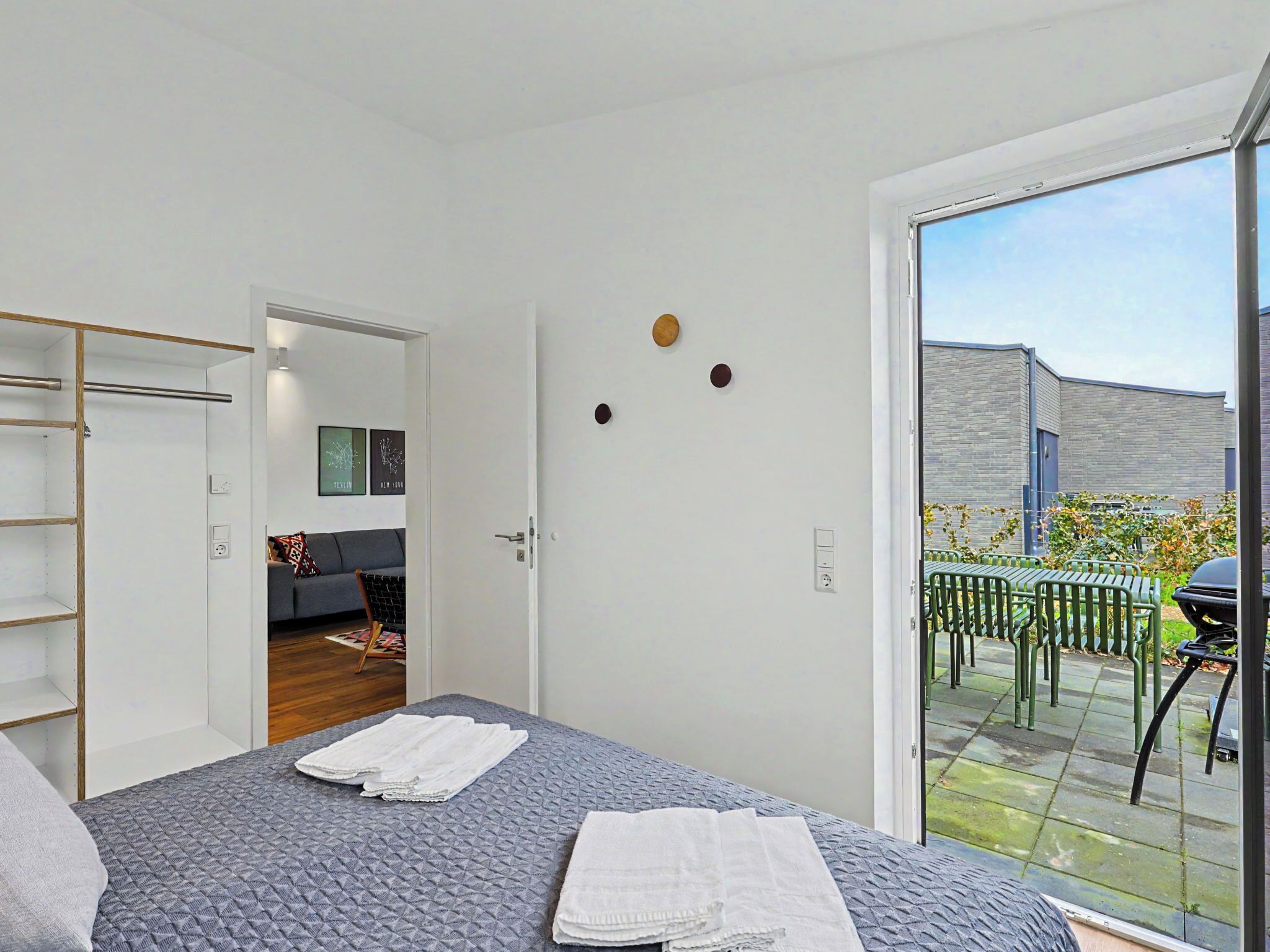 A bedroom with a bed, a wardrobe, a door leading to a living area, and a sliding glass door to an outdoor patio.