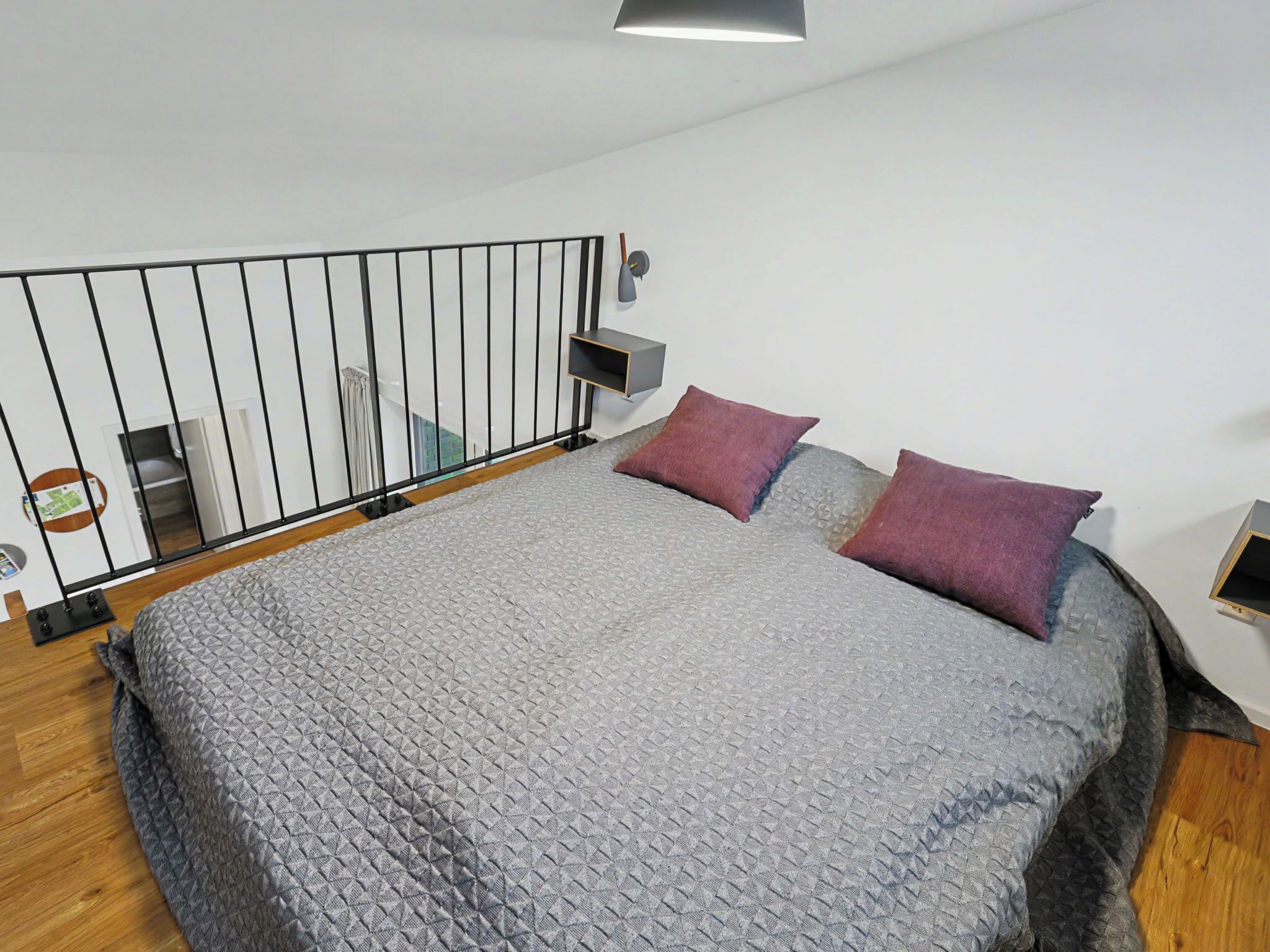 Un dormitorio con cama, dos almohadas, una mesita de noche, un estante en la pared y una barandilla.