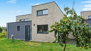 A modern two-story building with a flat roof, large windows, and a small tree with yellow fruit in the foreground. - Dünenblick 165 (Seenähe) by Interhome (Lembruch)
