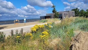 Blick auf die Küste mit einem modernen Gebäude, einem Sandstrand und einer Schaukel.