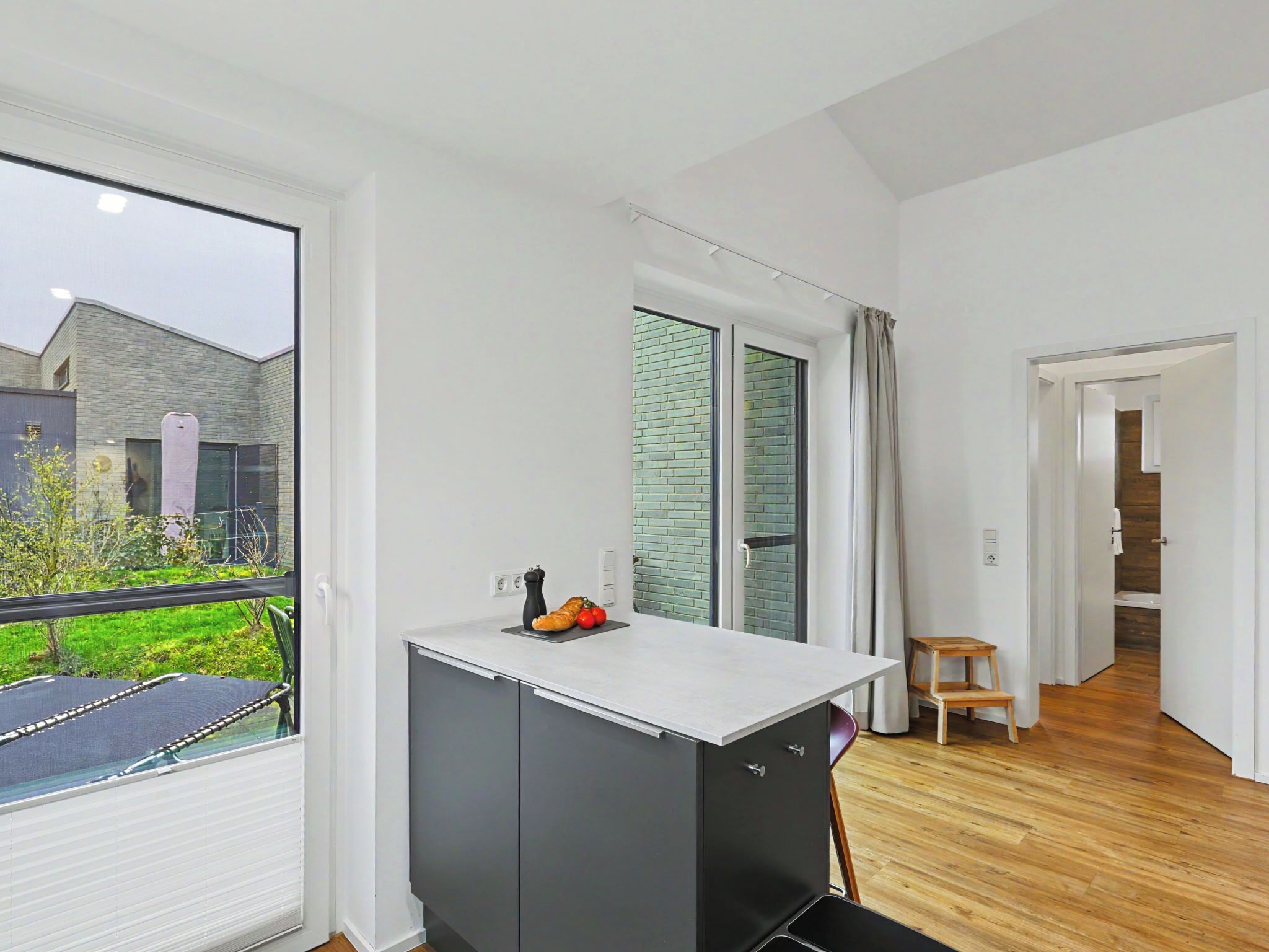 A modern kitchen with a large window, a small table, and a view of a garden.