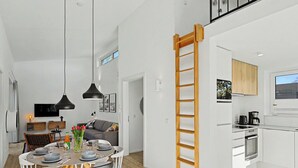 A modern kitchen with white cabinetry, a wooden ladder, and a dining area with a table and chairs.
