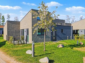 Een modern gebouw met een bakstenen gevel, grote ramen en een kleine boom in de voortuin.