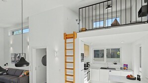 A modern apartment with a loft bedroom, a kitchen with a window, and a dining area with a table set for two.