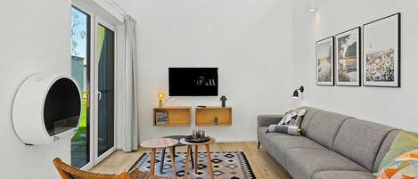 A modern living room with a sofa, a television, a wall-mounted shelf, and a patterned rug.