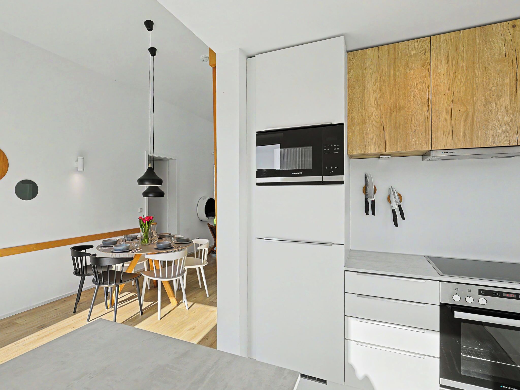 Una cuina moderna amb armaris blancs, un forn microones integrat i un forn d'acer inoxidable.