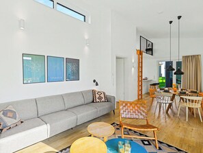 Ein modernes Wohnzimmer mit grauem Sofa, einem Essbereich mit Holztisch und -stühlen und einer Treppe, die zu einer oberen Ebene führt.