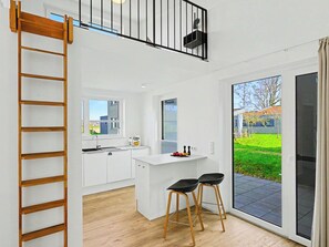 A modern kitchen with white cabinets, a wooden ladder, a small island with stools, and a sliding glass door leading to a garden. - Küstenzauber 282 by Interhome (Lembruch)