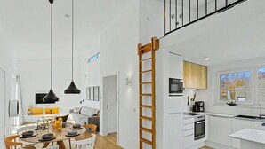 A modern kitchen with white cabinetry, a wooden ladder, and a dining area with a table and chairs. - Küstenzauber 282 by Interhome (Lembruch)