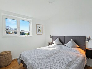 Ein Schlafzimmer mit Bett, Fenster, Wandlampe und einem gerahmten Bild.