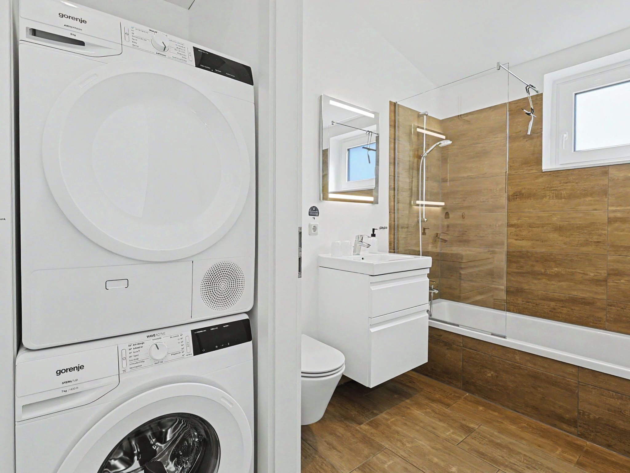 A modern bathroom with a washing machine, a toilet, a sink, and a shower.