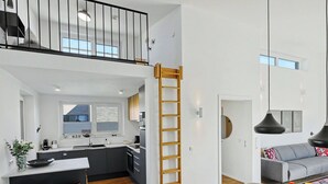 A modern kitchen with a central island, a dining area with a round table, and a loft bedroom with a balcony. - Lille Klit 325 by Interhome (Lembruch)