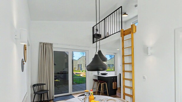 A modern dining area with a round table set for four, a black pendant light, and a view of the outdoors through a sliding glass door. - Lille Klit 325 by Interhome (Lembruch)