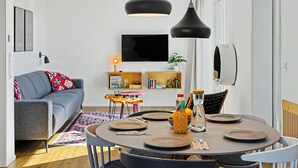 A modern living room with a sofa, a dining table set for four, and a TV mounted on the wall. - Lille Klit 325 by Interhome (Lembruch)