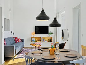 A modern living room with a sofa, a dining table set for four, and a TV mounted on the wall. - Lille Klit (325) by Interhome (Lembruch)