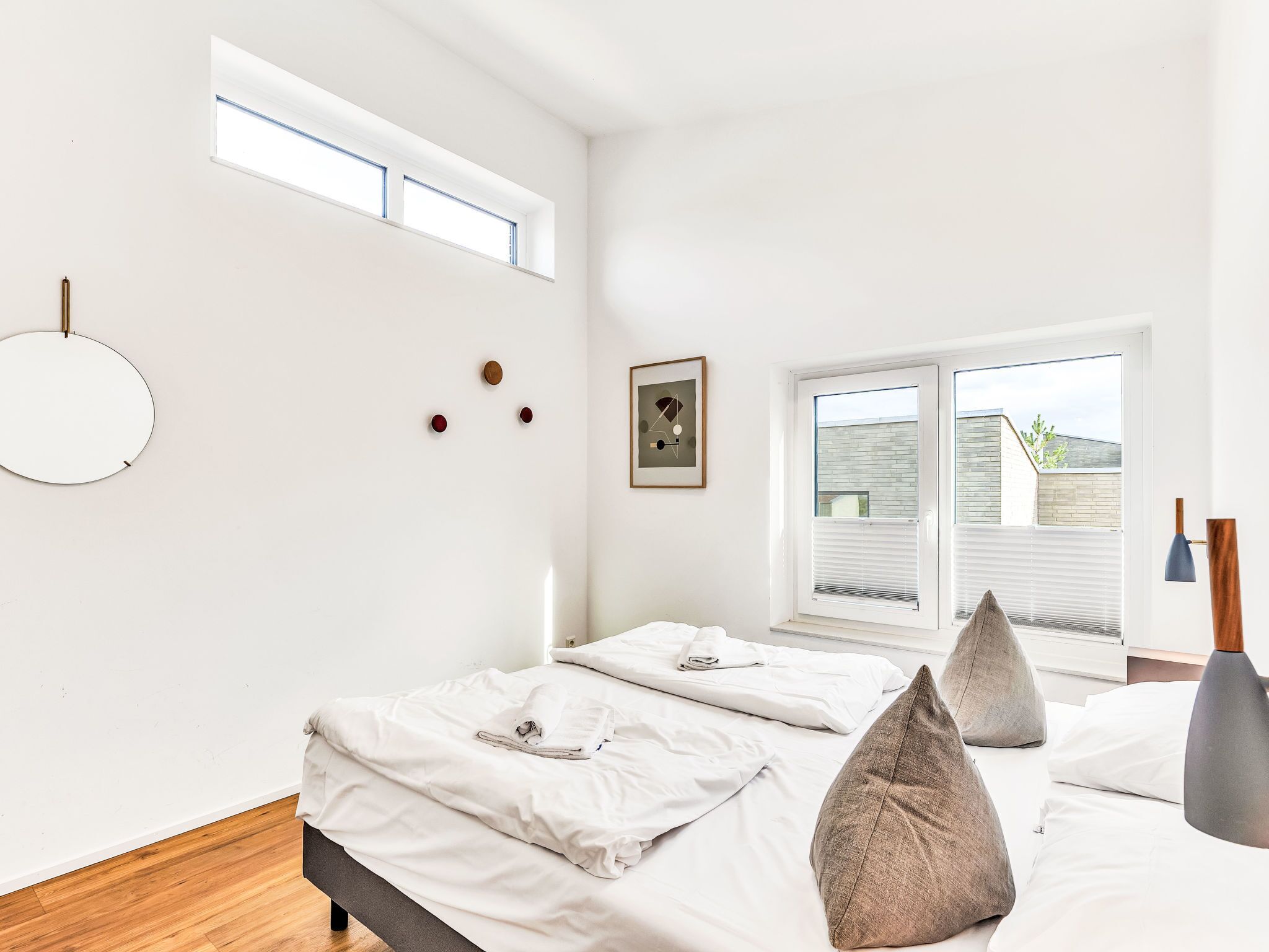 Een moderne slaapkamer met een groot bed, dakraam, ronde spiegel en een lijst met een afbeelding.