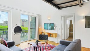 A modern living room with a sofa, a small table, a TV, and a sliding glass door leading to an outdoor area. - Dümmersee Lodge 147 by Interhome (Lembruch)