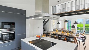 A modern kitchen with a central island, built-in oven, and a dining area with a view of the outdoors. - Dümmersee Lodge 147 by Interhome (Lembruch)