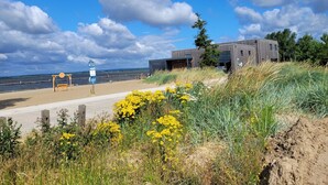 A coastal view with a modern building, a sandy beach, and a swing set.
