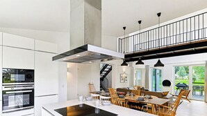 A modern kitchen with a central island, built-in oven, and a staircase leading to an upper level.