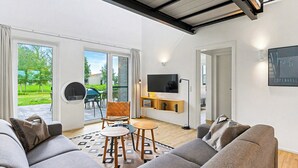 A modern living room with a sofa set, a TV mounted on the wall, and a dining area with chairs and a table.