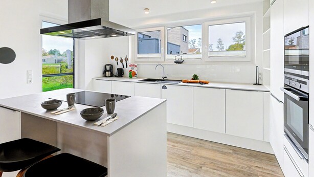 A modern kitchen with white cabinetry, a large island, and a built-in oven.