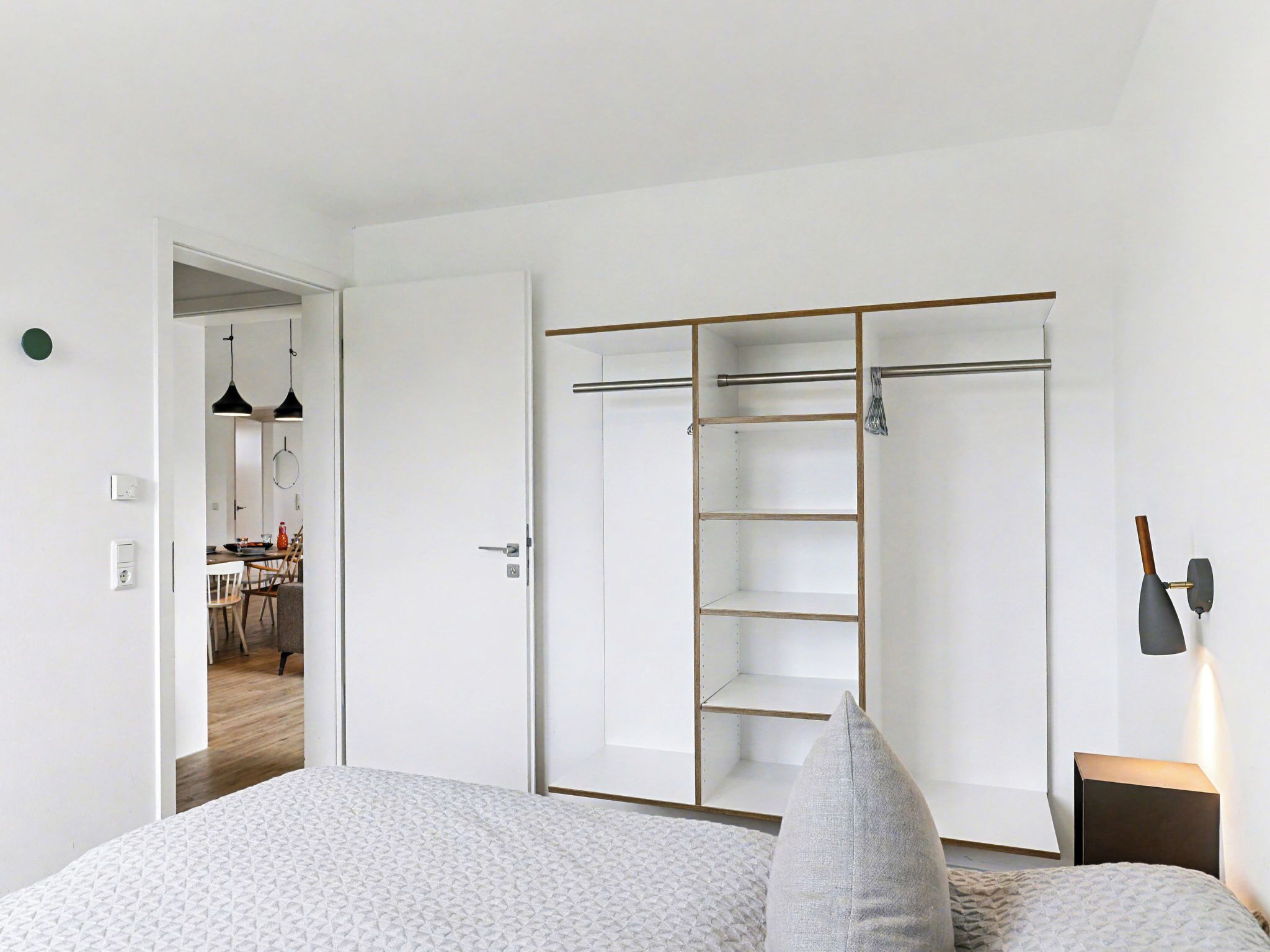 A bedroom with a bed, a wardrobe with a mirror, and a nightstand with a lamp.