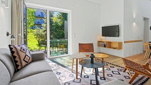 Una sala de estar moderna con un sofá, una mesita, una silla, un televisor y una puerta corrediza de vidrio que da a un balcón.
