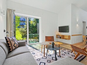 A modern living room with a sofa, a small table, a chair, a TV, and a sliding glass door leading to a balcony. - Lichtblick by Interhome (Lembruch)