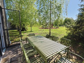 Eine Terrasse im Freien mit Tisch und Stühlen, umgeben von Bäumen und einer Rasenfläche.