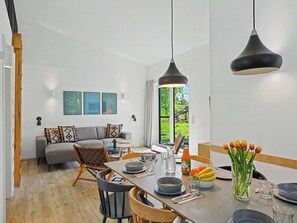 Ein modernes Wohnzimmer mit einer Couch, einem Esstisch, Stühlen, einem Fenster mit Blick und Wandbildern.
