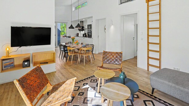 Una sala moderna con televisor, asientos, comedor y una escalera.