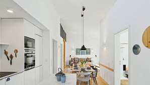 Una cocina moderna con electrodomésticos integrados, un comedor con mesa y sillas de madera, y un pasillo que da a otras habitaciones.