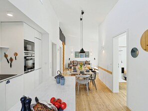 A modern kitchen with built-in appliances, a dining area with a wooden table and chairs, and a hallway leading to other rooms. - Lichtblick by Interhome (Lembruch)