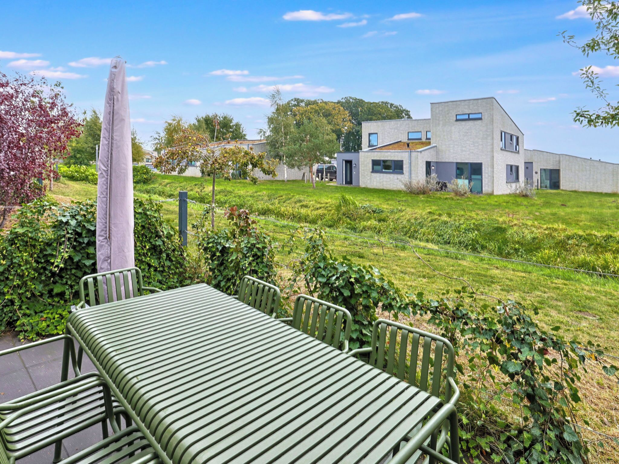 A modern building with a flat roof and large windows, surrounded by a grassy area with a metal table and chairs.