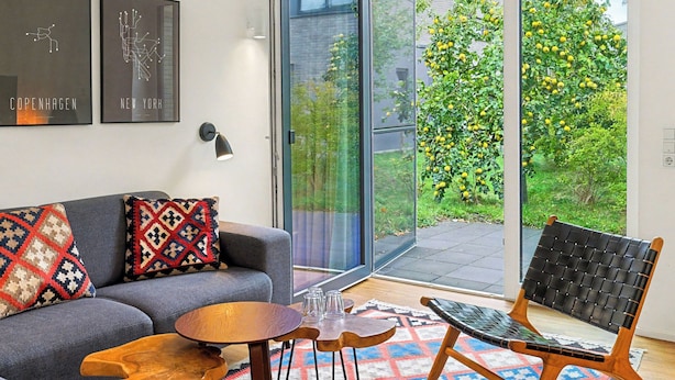 Ein modernes Wohnzimmer mit einem grauen Sofa, gemusterten Kissen, einem Holztisch und einem schwarzen Gewebestuhl.