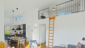 Un intérieur moderne comprenant un espace repas, une cuisine et un salon, avec une chambre en mezzanine accessible par une échelle en bois.