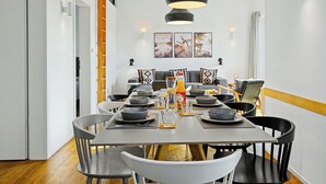 Un coin repas avec une table dressée pour quatre personnes, des chaises, une suspension et un escalier doté d’une rampe.