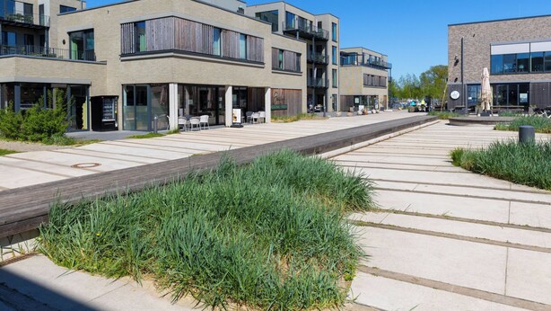 En modern stadsgata med samtida byggnader, uteserveringar och en gångbana för fotgängare.