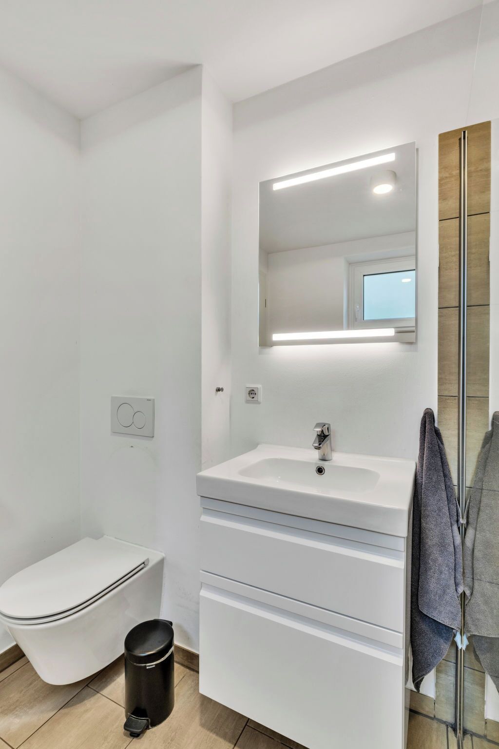 A modern bathroom with a white sink, mirror, and toilet.
