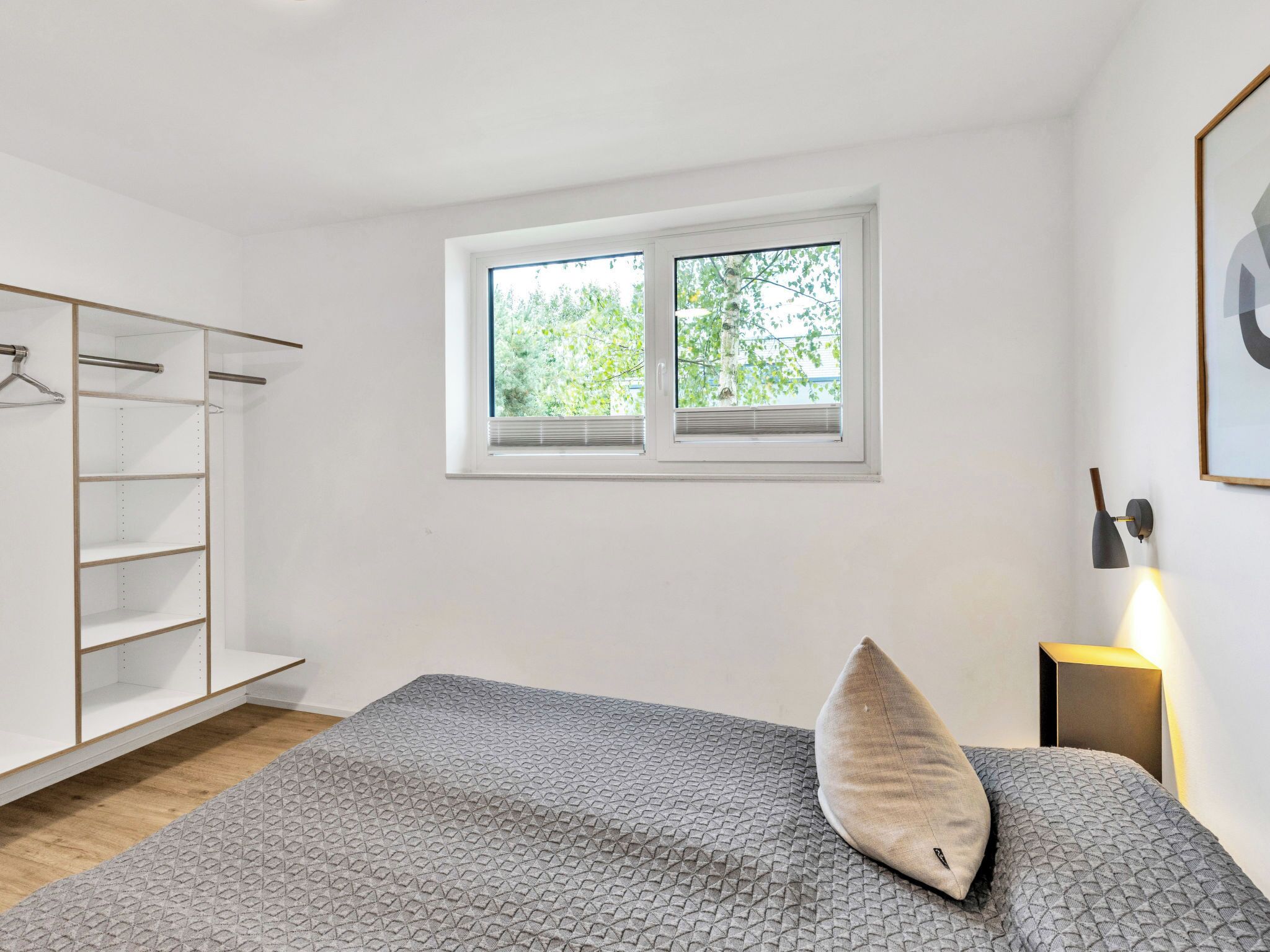 Un dormitorio con cama, ventana, armario y mesita de noche.