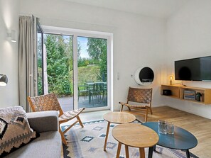 A modern living room with a sofa, two chairs, a coffee table, a TV, and a sliding glass door leading to an outdoor area with greenery. - Morgentau by Interhome (Lembruch)