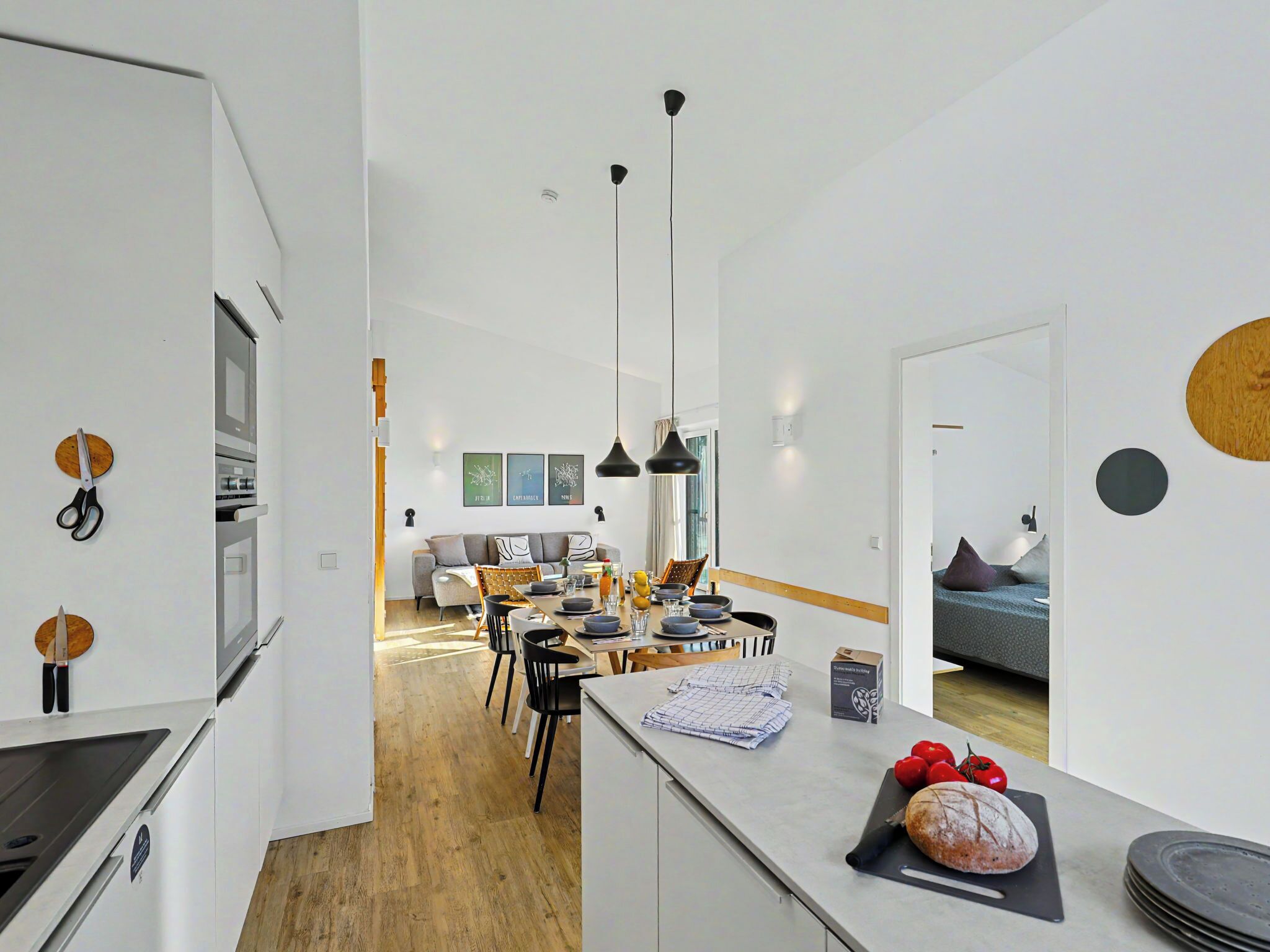 A modern kitchen with a dining area, wooden flooring, and a view into the living room.