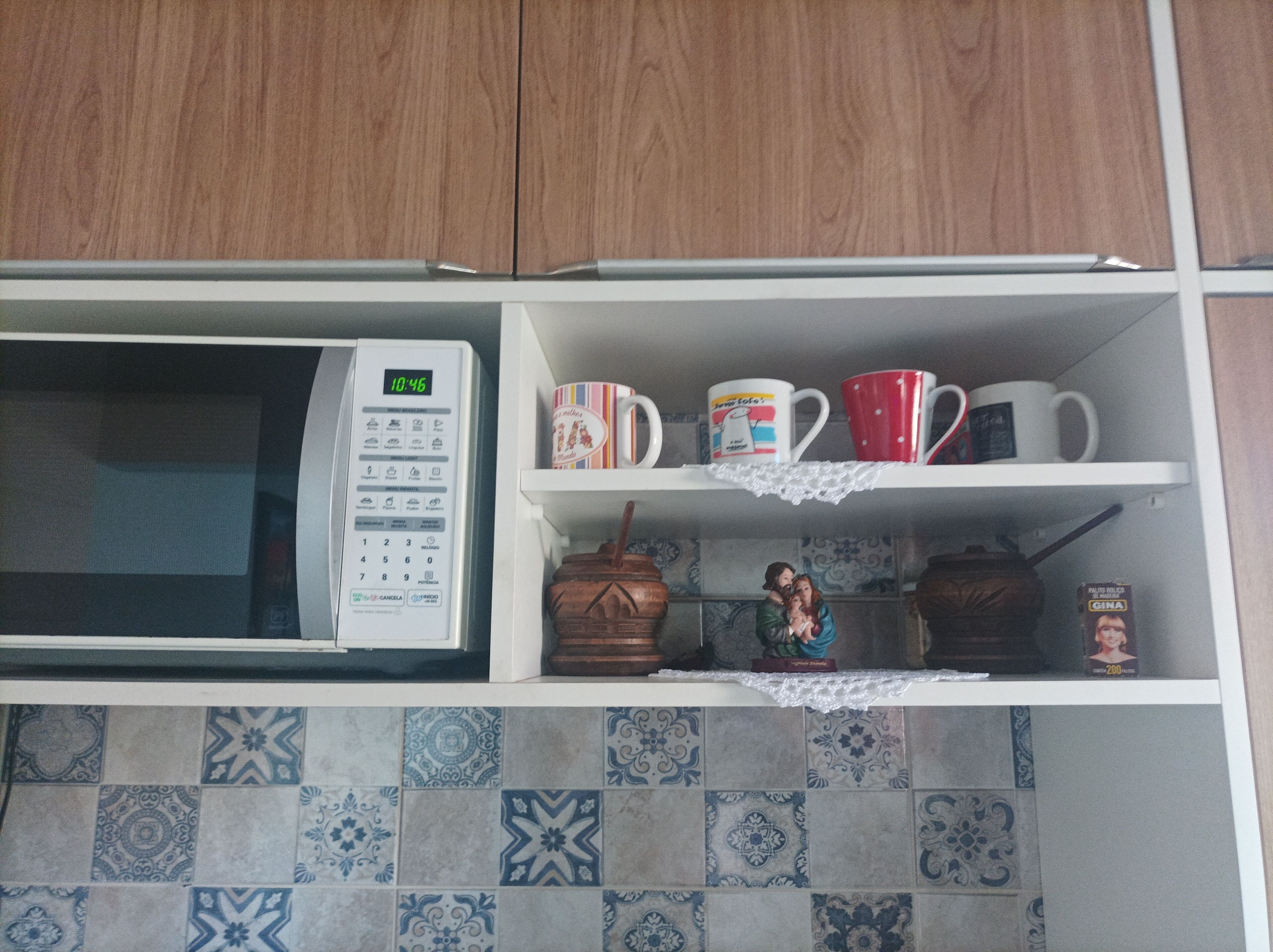 A kitchen with a microwave, a shelf with mugs, and a decorative figure.
