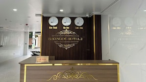 Un mostrador de recepción de hotel con detalles de madera y detalles dorados, que incluye relojes y un letrero que dice "BAONGOC HOTEL 2".
