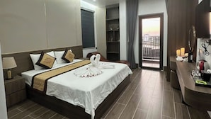 Una habitación de hotel con una cama grande, una mesita de noche, un escritorio y vistas a la ciudad desde un balcón.
