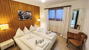 Ein Hotelzimmer mit zwei Betten, einer Holzvertäfelung, einem Fenster mit Vorhängen, einem Holzstuhl und einer Wandlampe.
