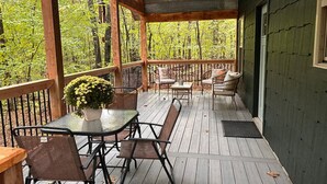 Eine überdachte Terrasse mit Gartenmöbeln, einem Tisch mit Topfpflanze und Blick auf ein bewaldetes Gebiet.