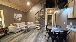 Uma sala de estar ampla com teto de madeira, escada, mesa de jantar com cadeiras e um sofá.