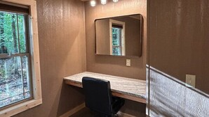 Ein kleiner, kompakter Raum mit einem einzelnen Schreibtisch, einem Stuhl, einem großen Spiegel und einem Fenster.